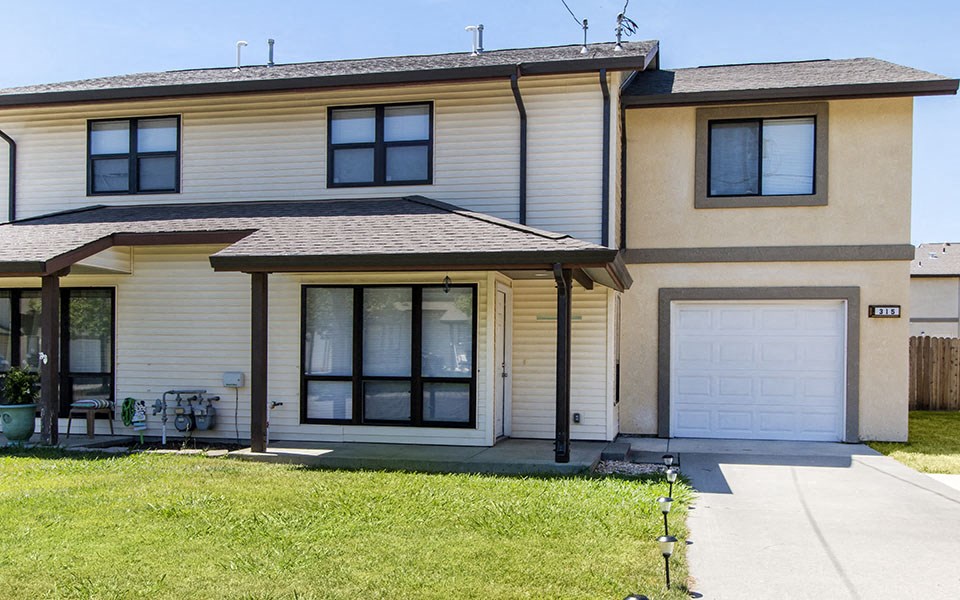 a yellow house with a white garage and a lawn