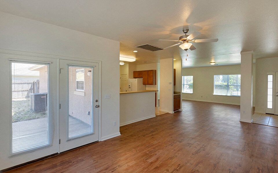an empty living room with a door to the kitchen and a ceiling fan