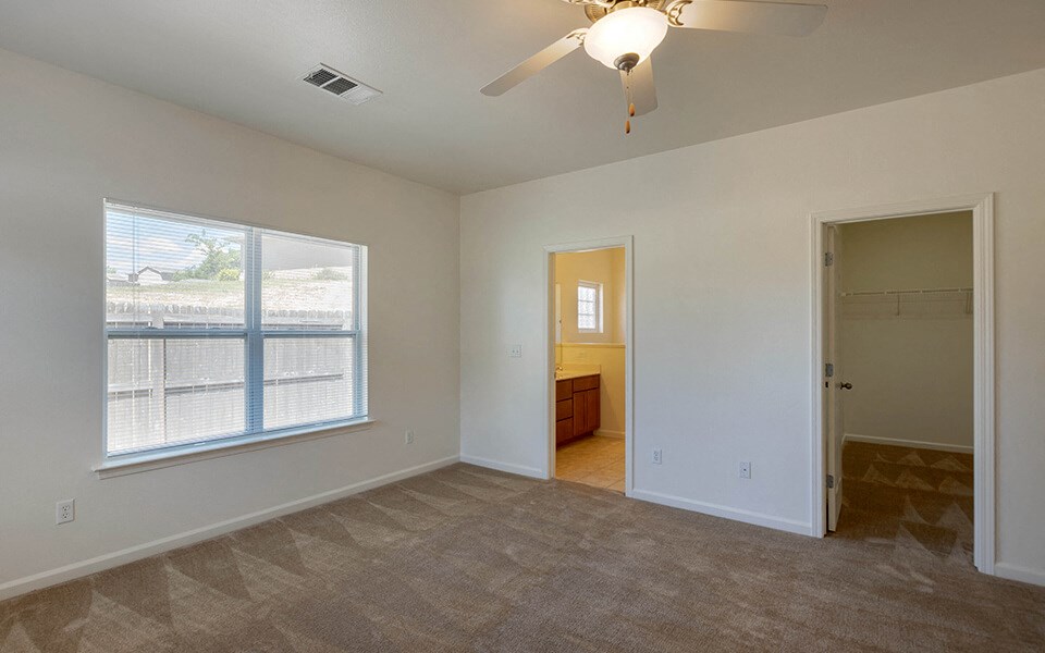 an empty living room with a large window and a ceiling fan