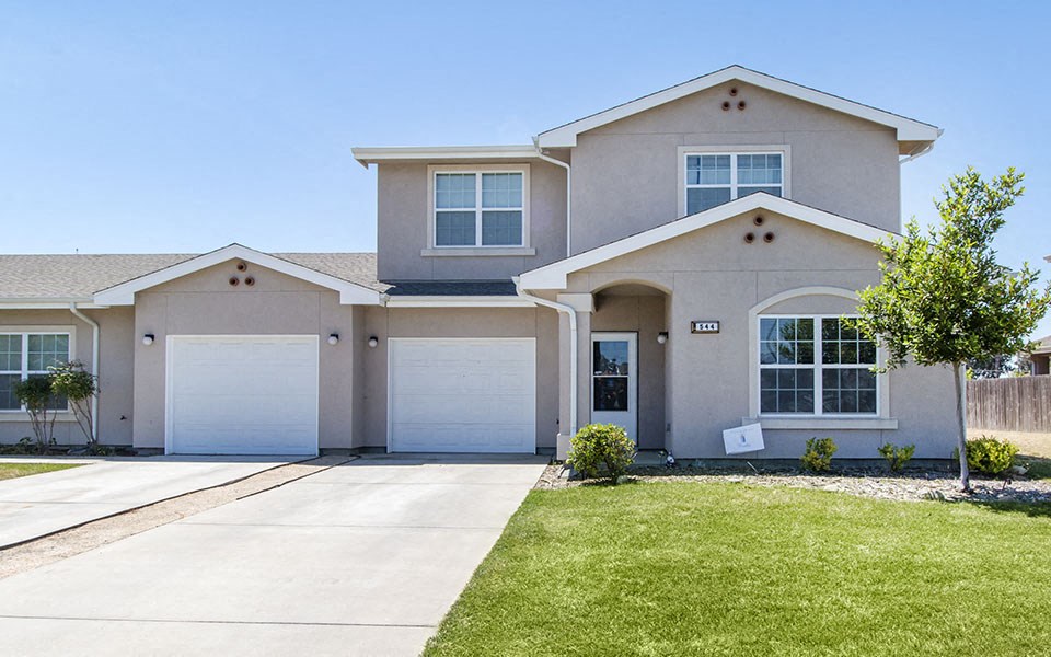 a beige house with two garage doors and a lawn