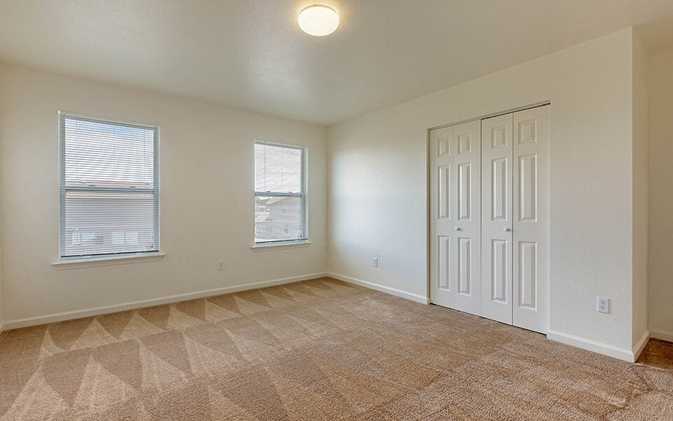 an empty living room with a door and two windows