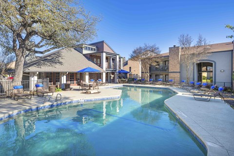 A large swimming pool surrounded by a patio with chairs and umbrellas.