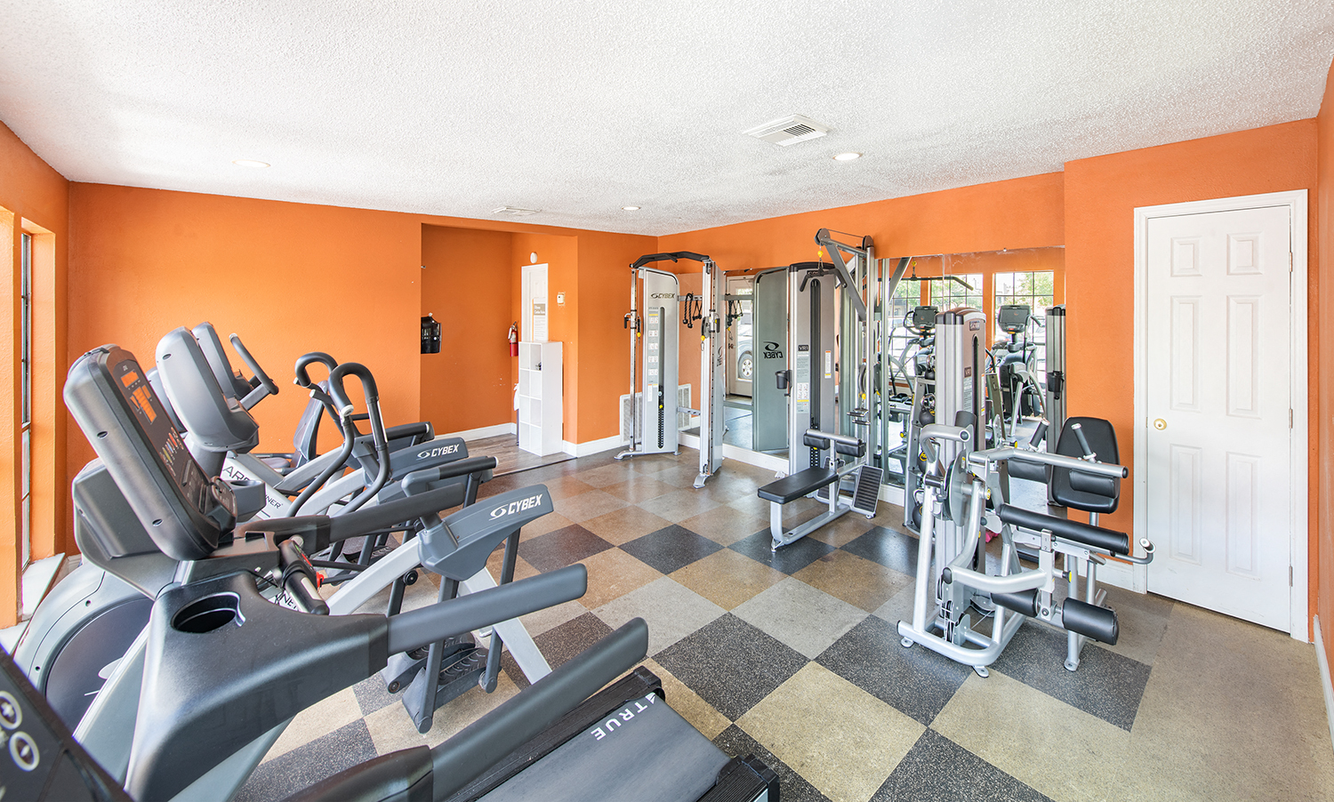 a gym with weights and cardio equipment in a room with a door