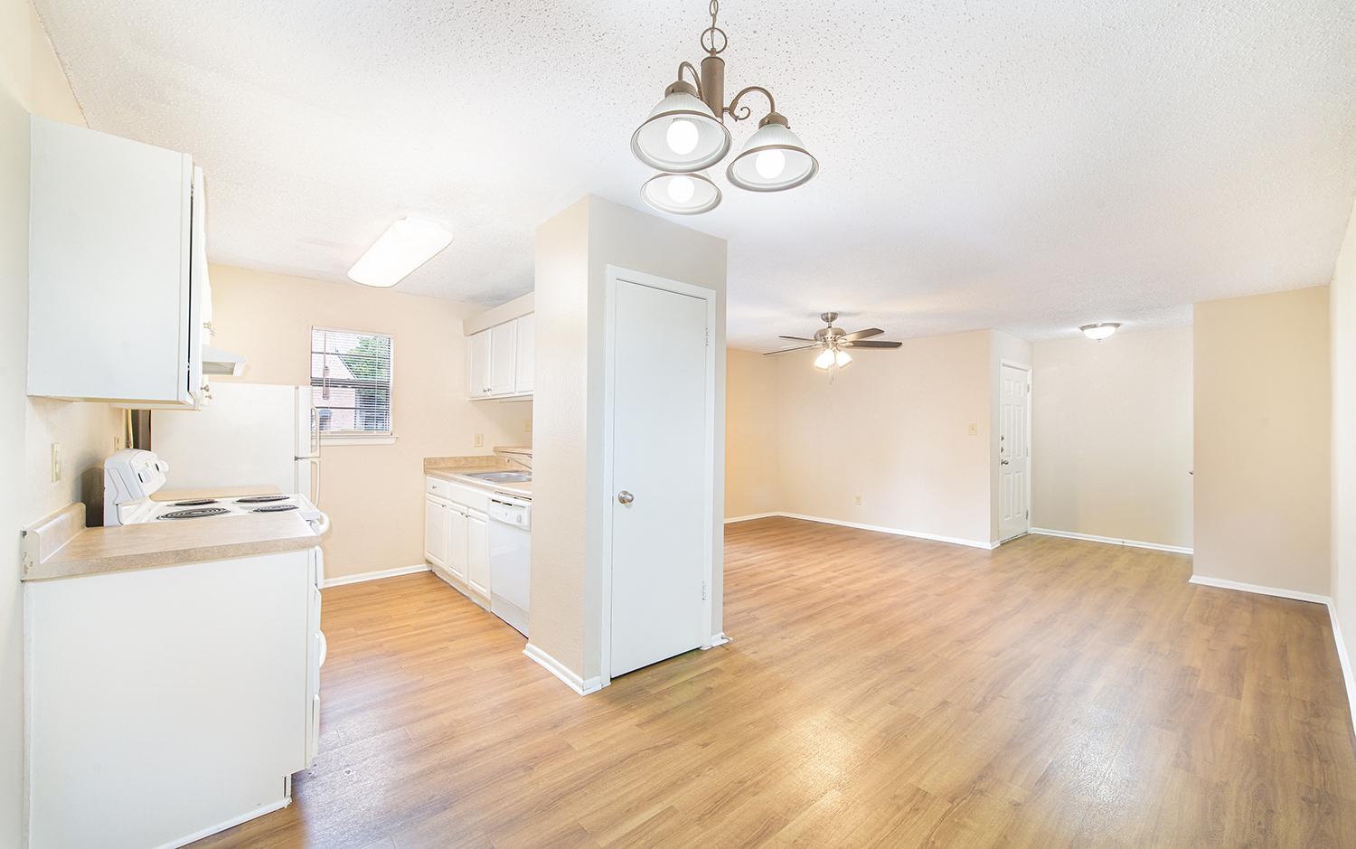 an empty living room and kitchen with a wood floor and white cabinets
