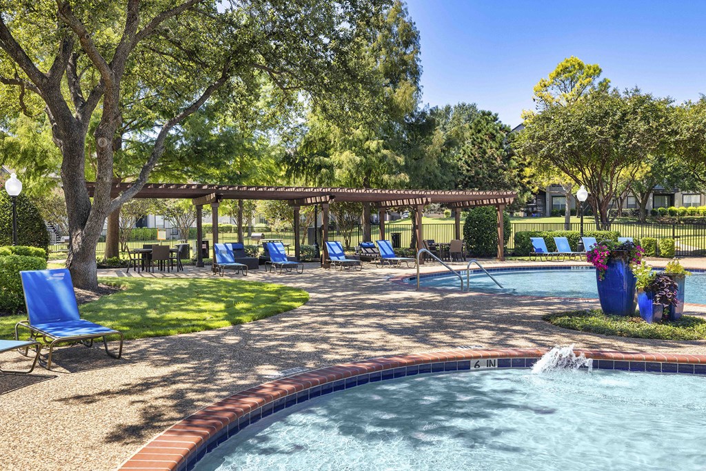 A pool with a waterfall and a pavilion in the background.