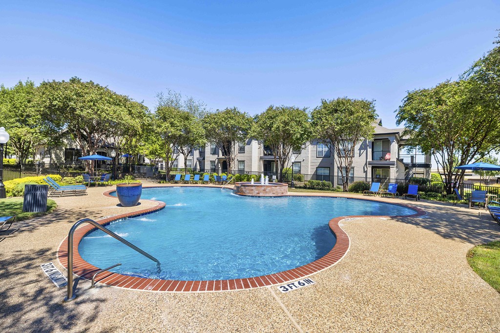 A swimming pool surrounded by a brick border and a grassy area with trees.