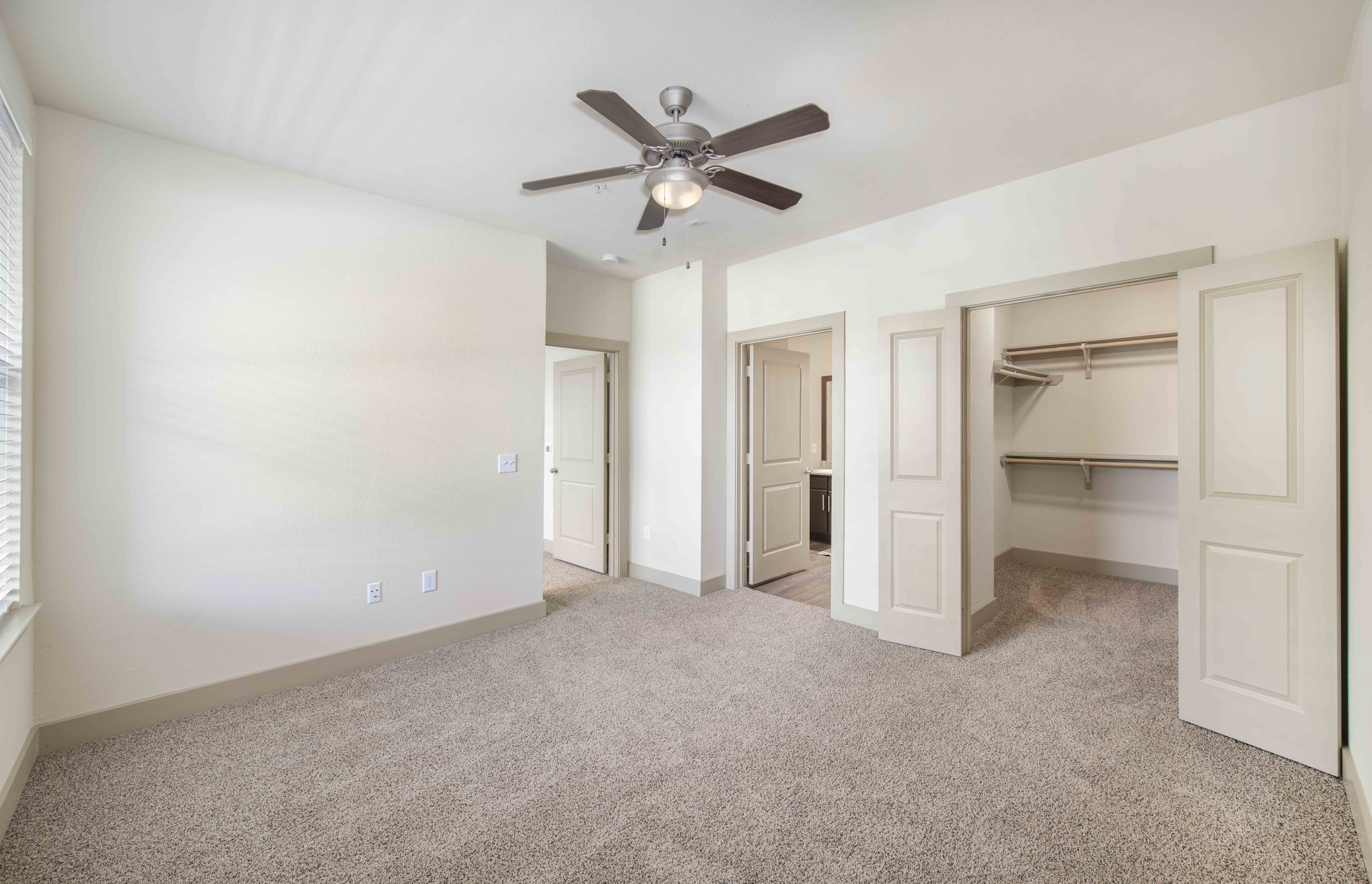 an empty bedroom with a ceiling fan and closet