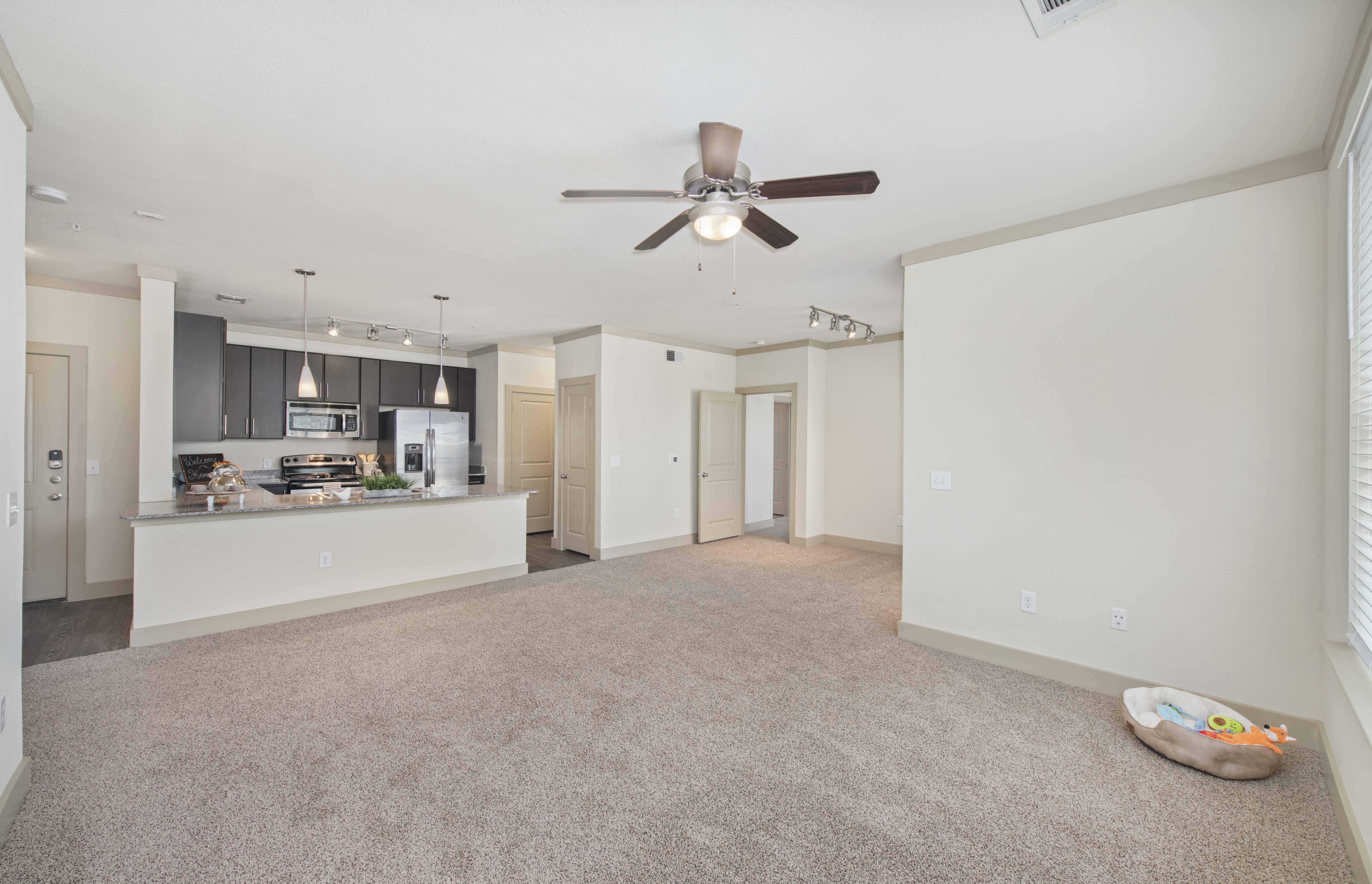 an empty living room with a ceiling fan and a kitchen