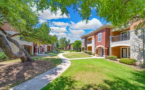 a pathway between two buildings with grass and trees