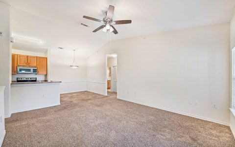 an empty living room with a ceiling fan and a kitchen
