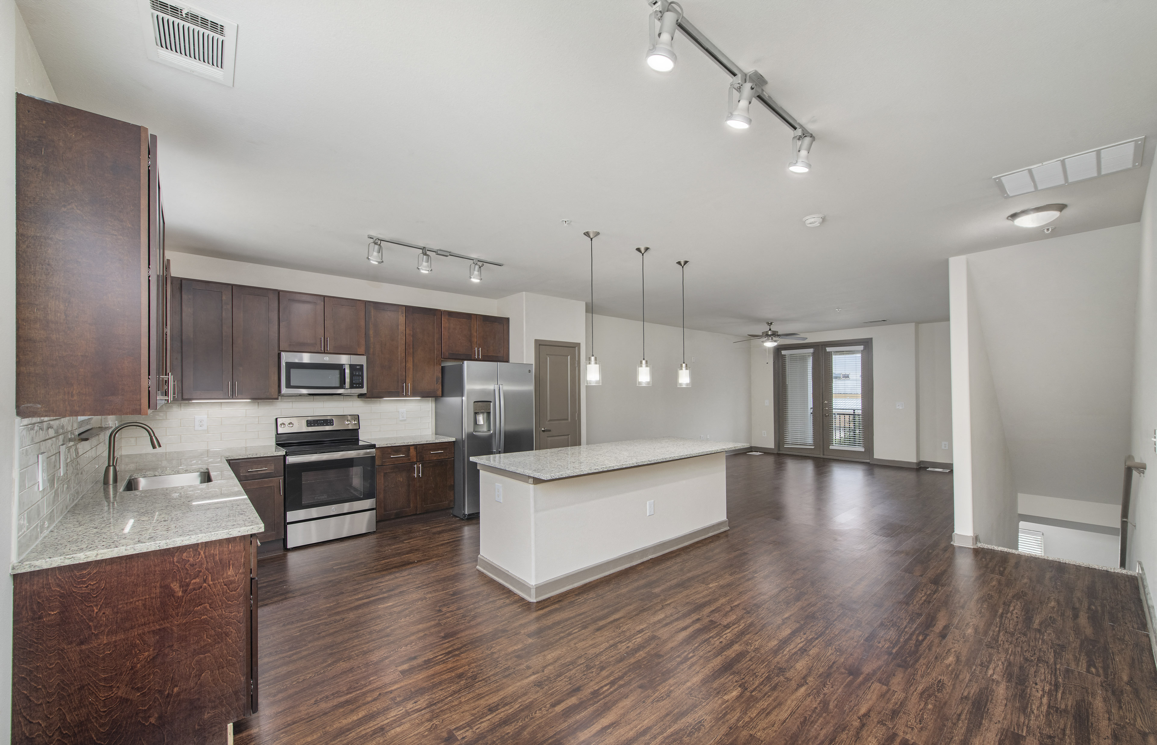 an open kitchen and living room with wood flooring and stainless steel appliances