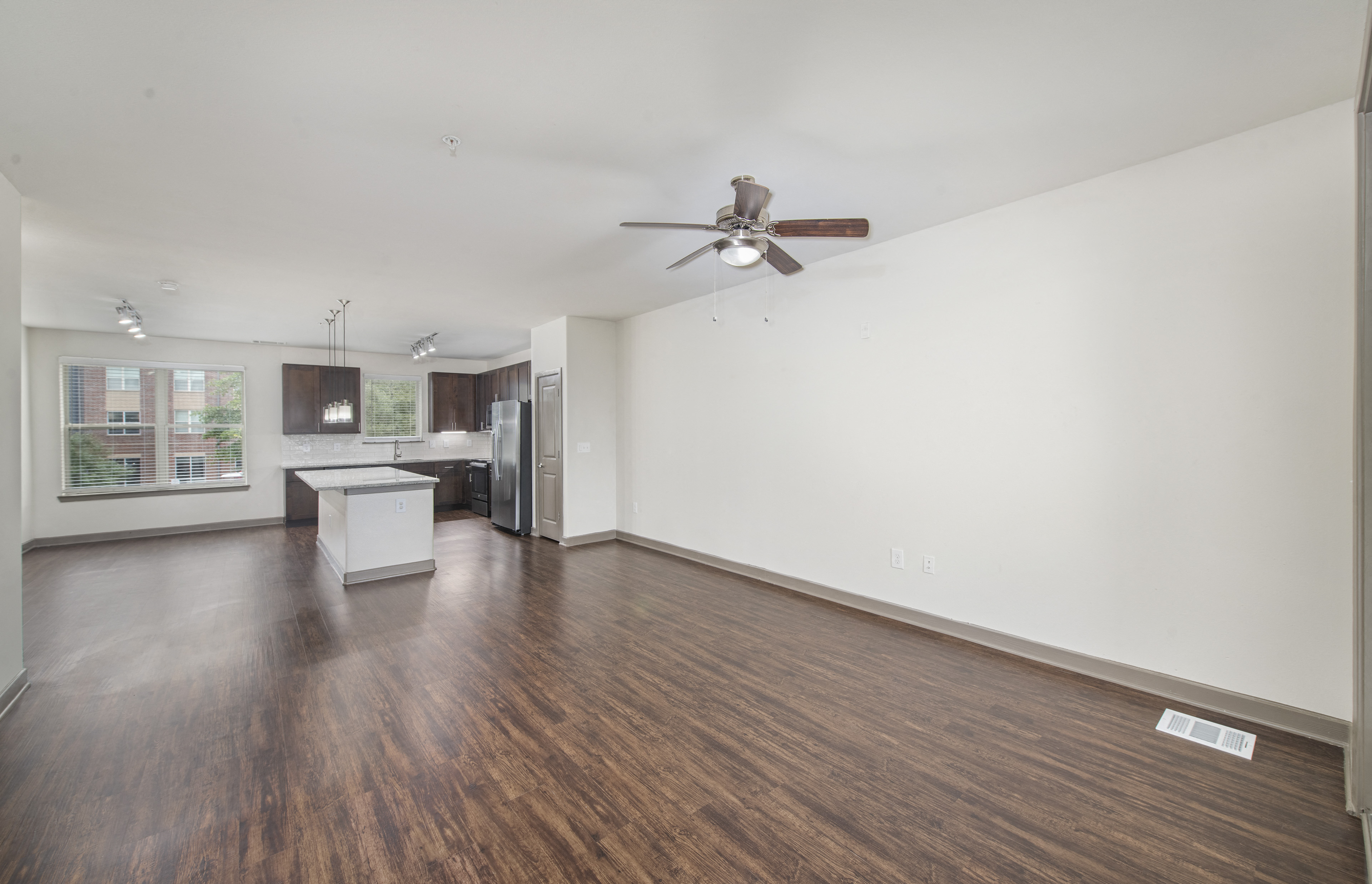 an empty living room with a ceiling fan and a kitchen