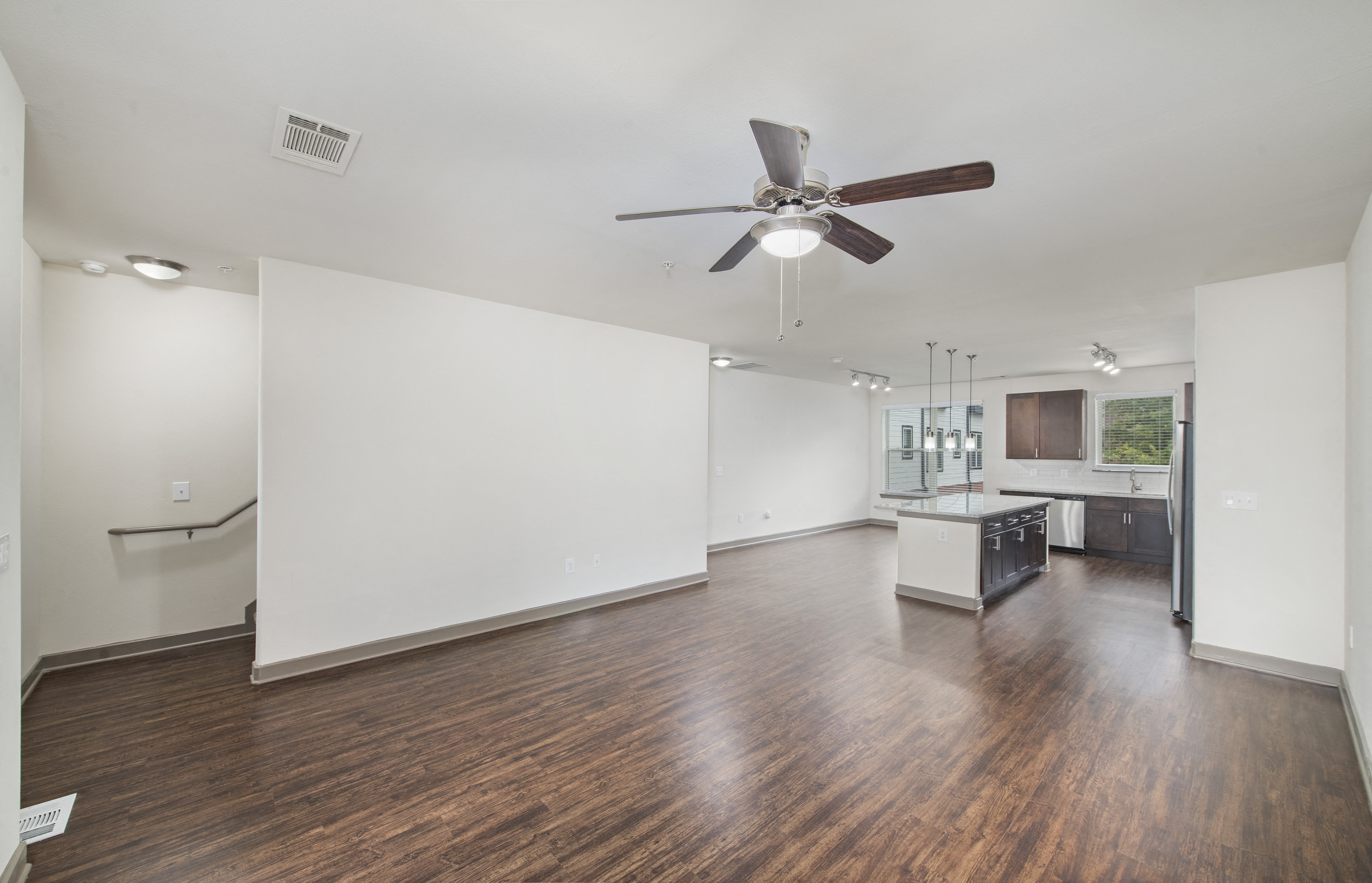 an empty living room with a ceiling fan and a kitchen