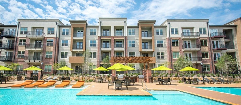 a swimming pool with yellow umbrellas in front of an apartment building