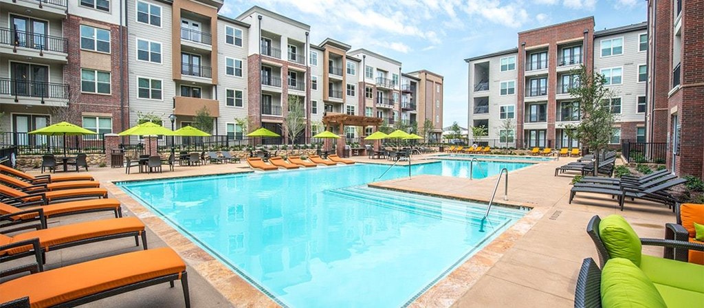 a swimming pool with chairs and umbrellas in front of an apartment building