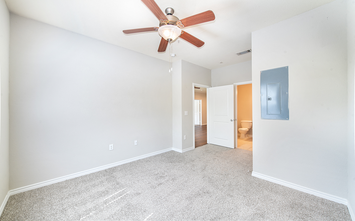 an empty living room with a ceiling fan and a door to a bathroom