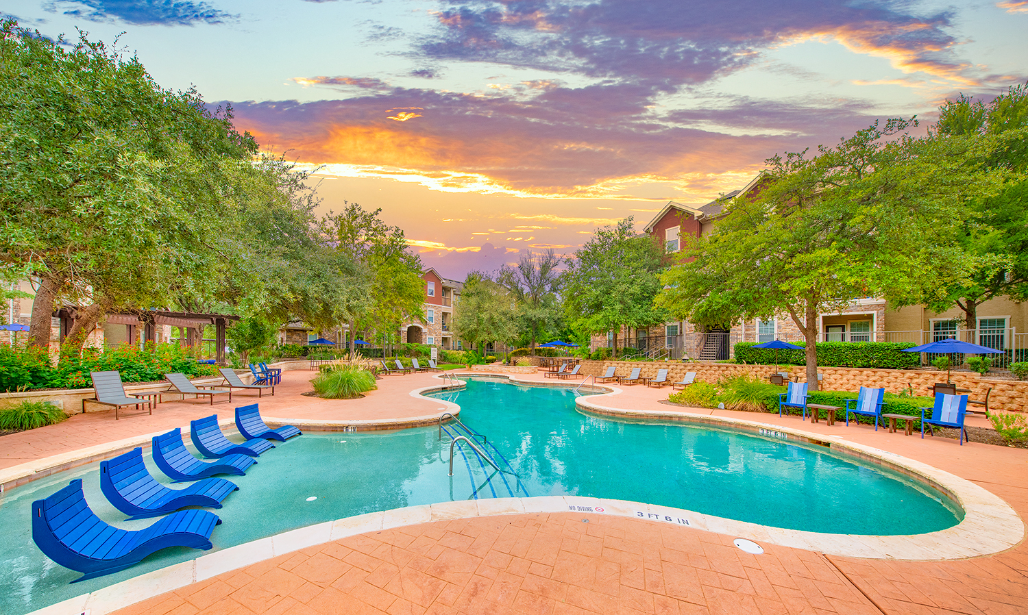 a swimming pool with blue lounge chairs at sunset