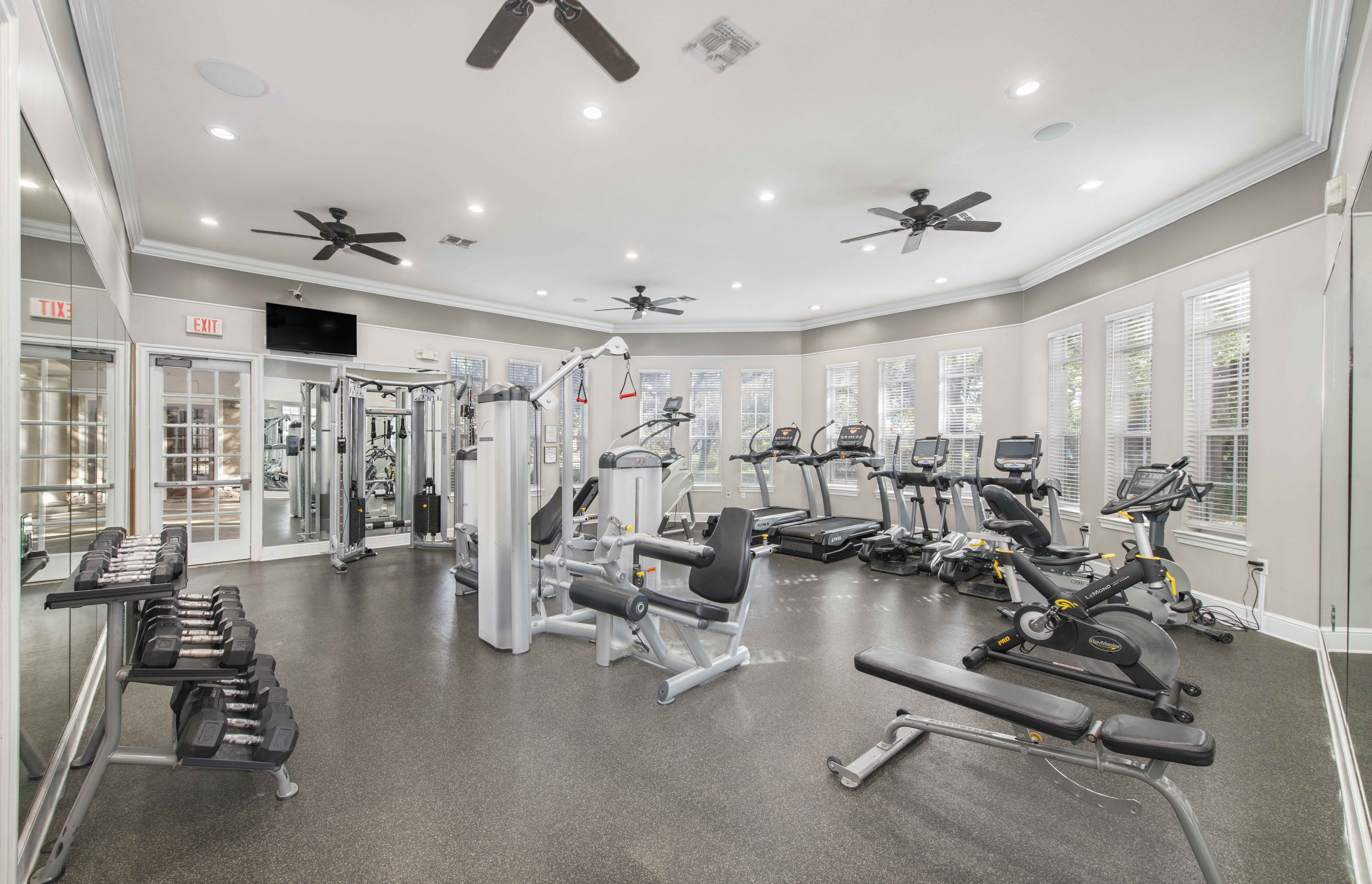 a gym with weights and cardio machines and ceiling fans