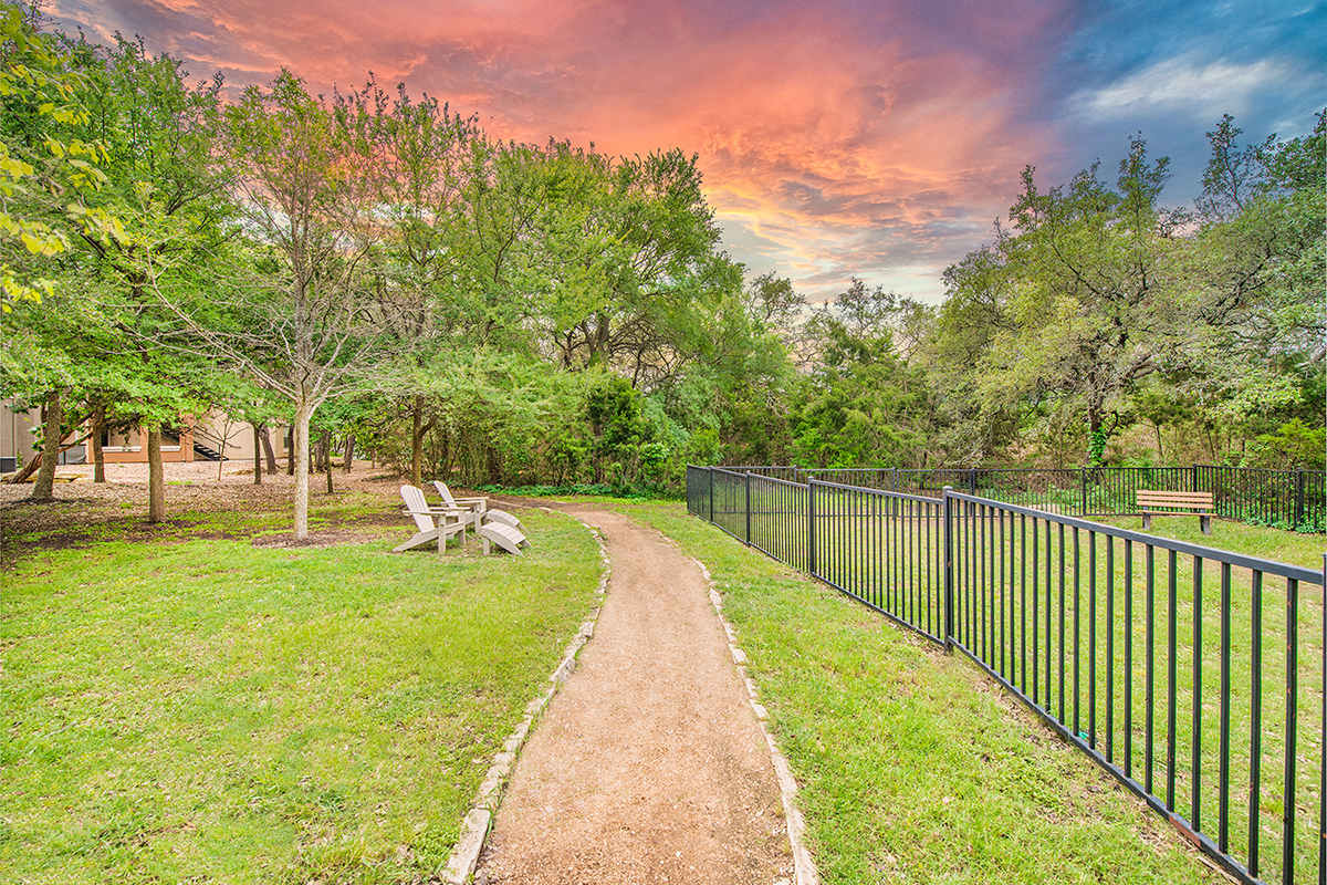 a path leading to a park with benches and a fence