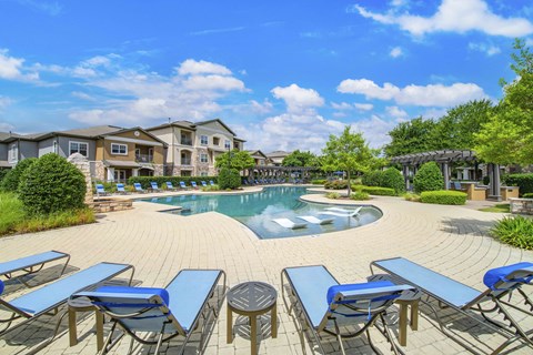 A pool surrounded by blue lounge chairs and a clear sky.