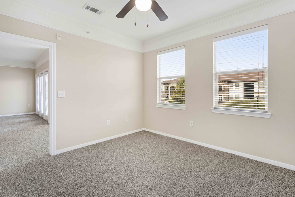 A room with a ceiling fan and two windows.