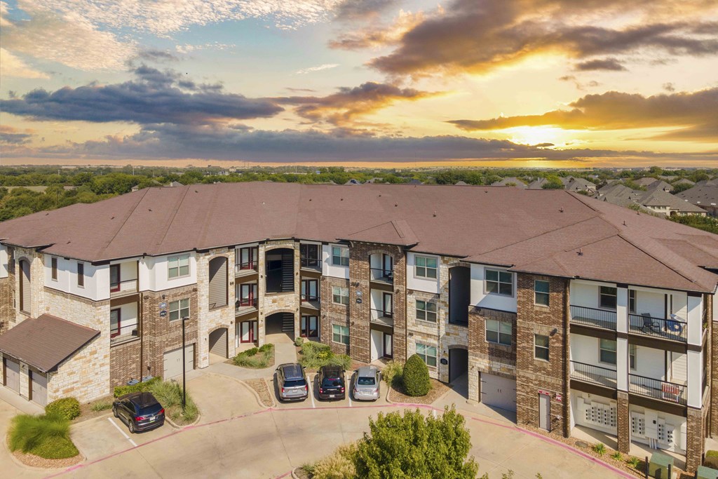 A sunset view of a large apartment complex with cars parked in the driveway.