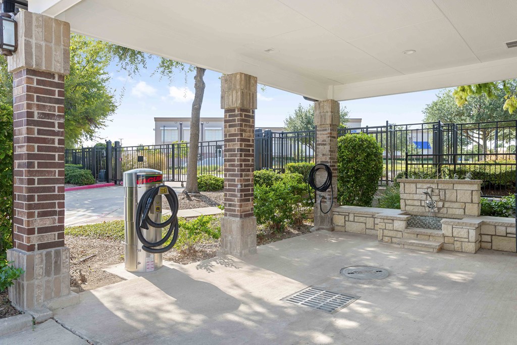 A parking area with a brick pillar and a black fence.
