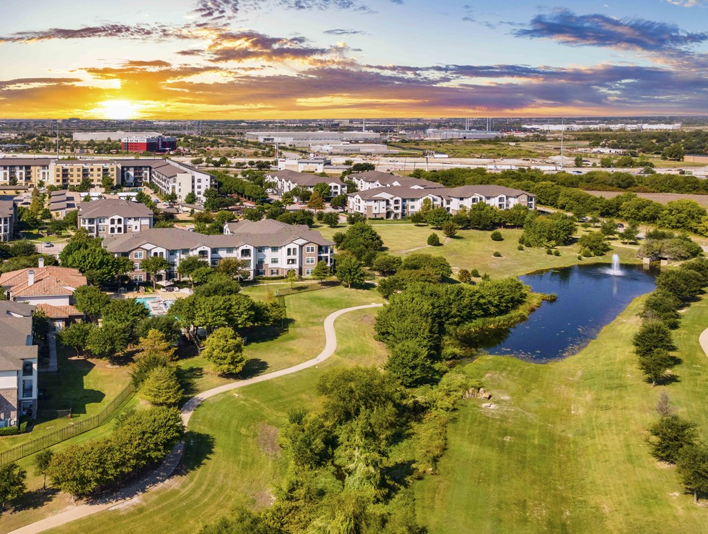 A sunset view of a residential area with a pond and greenery.