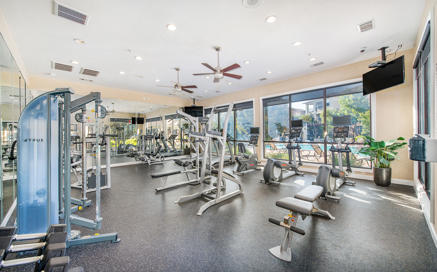 a gym with cardio machines and a window view of a pool