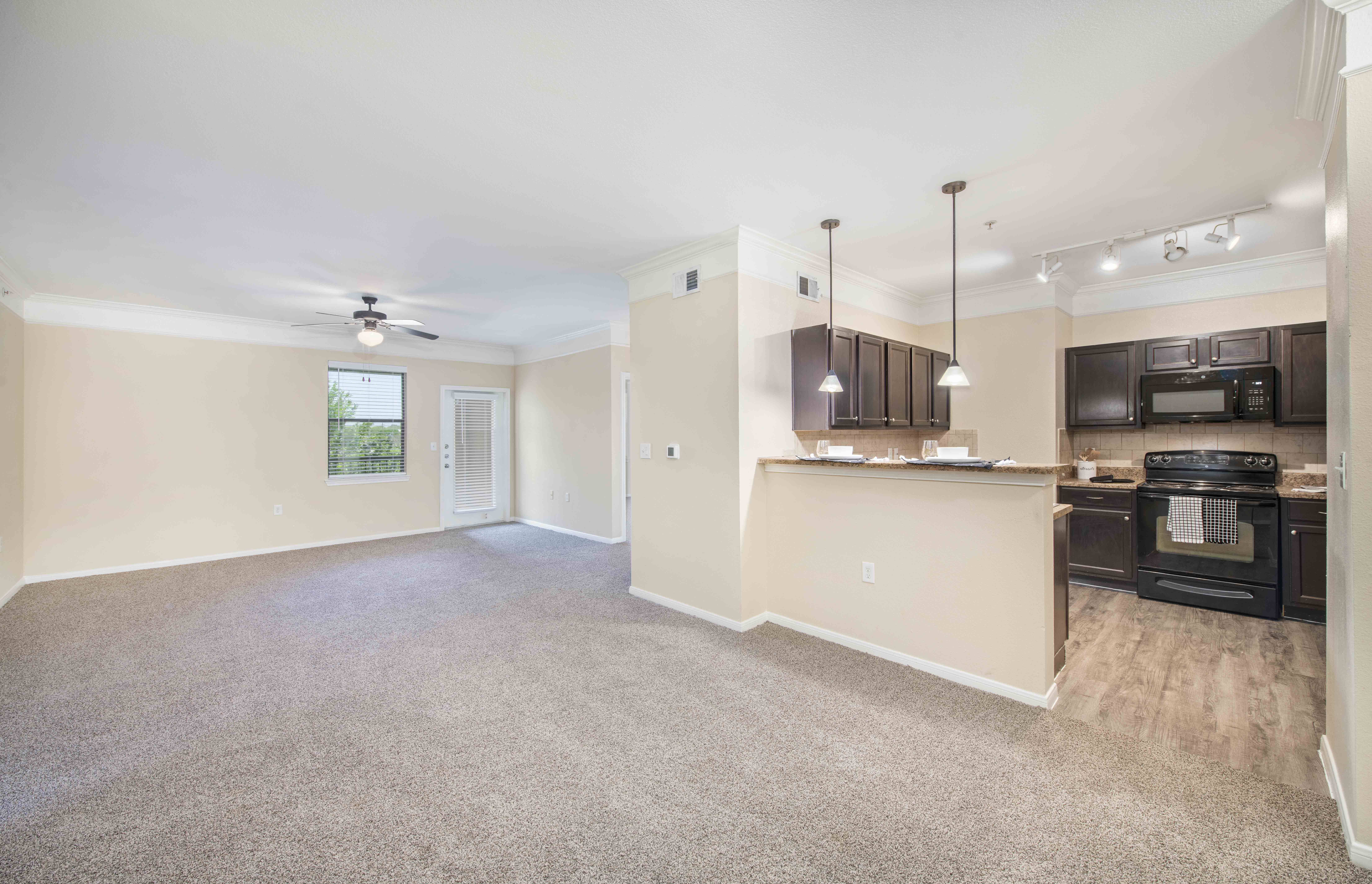 an empty living room with a kitchen and a ceiling fan