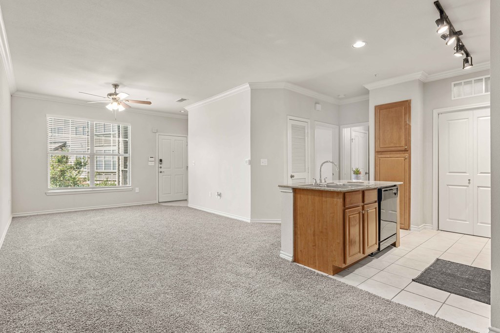 an empty living room with a kitchen and a ceiling fan
