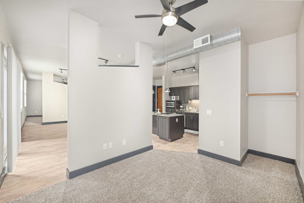 an empty living room with a ceiling fan and a kitchen