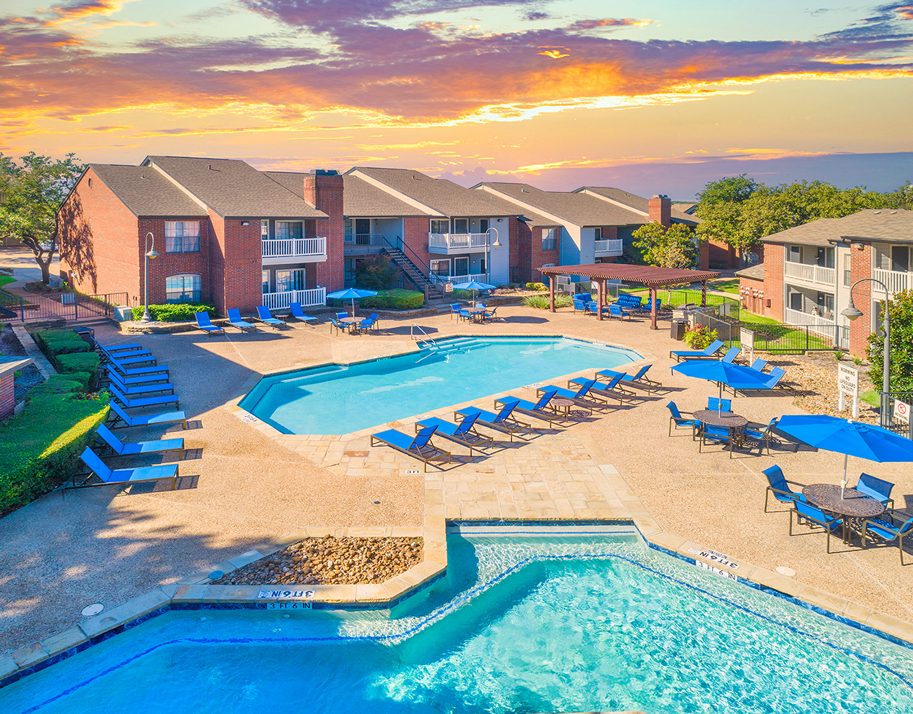 an aerial view of a swimming pool with chairs and umbrellas at sunset