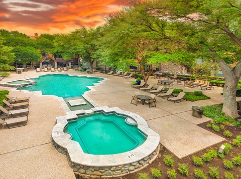 a swimming pool with a poolside hot tub and a patio with chairs and trees