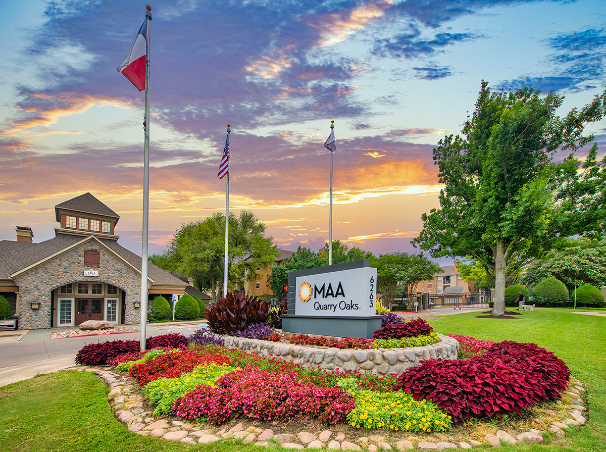 the front of a building with flags and a sign and flowers