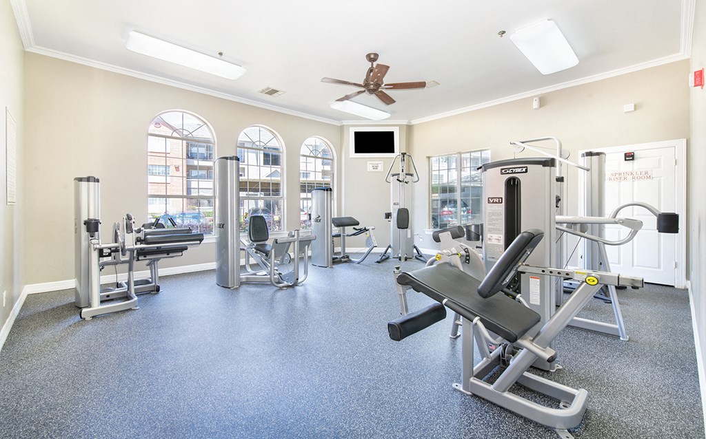 a fitness room with cardio equipment and windows