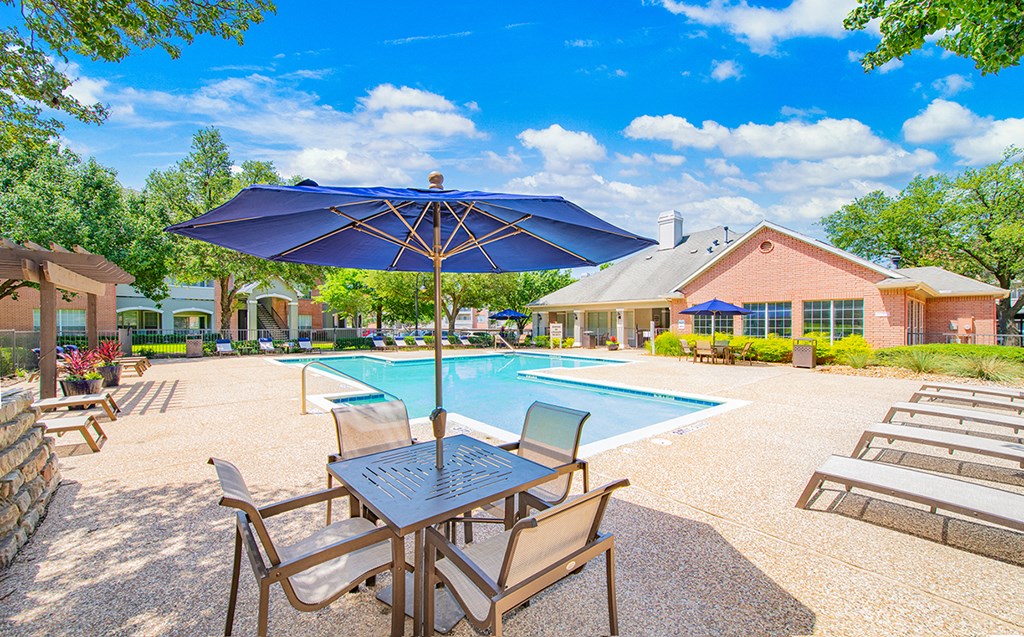 our resort style swimming pool is surrounded by patio furniture and umbrellas