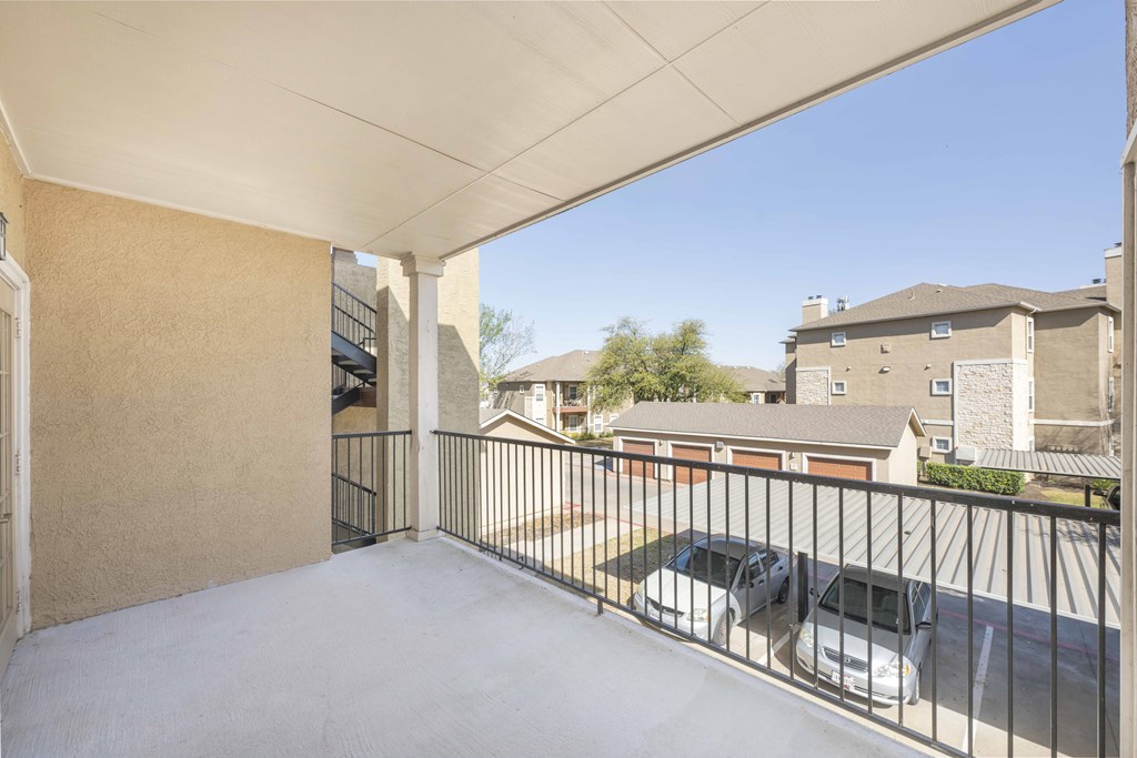 A balcony with a white railing and a car parked in the driveway.