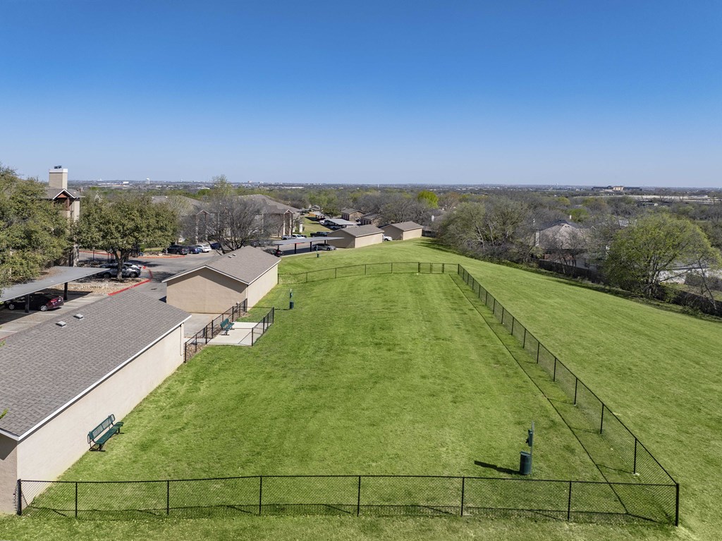 A large grassy field with a fence and a building in the background.