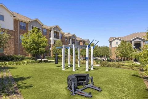 A gym set up in a grassy area in front of apartment buildings.