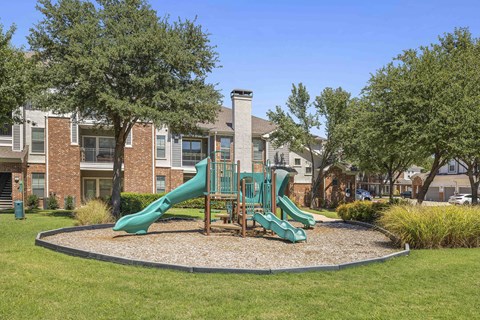 A playground with a green slide and a red brick building in the background.