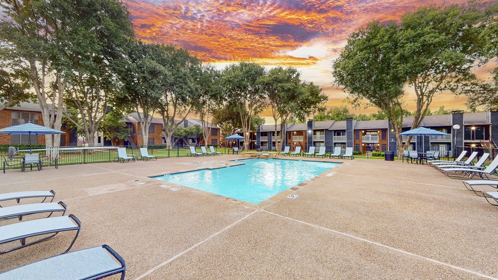 A sunset view of a pool area with lounge chairs and umbrellas.