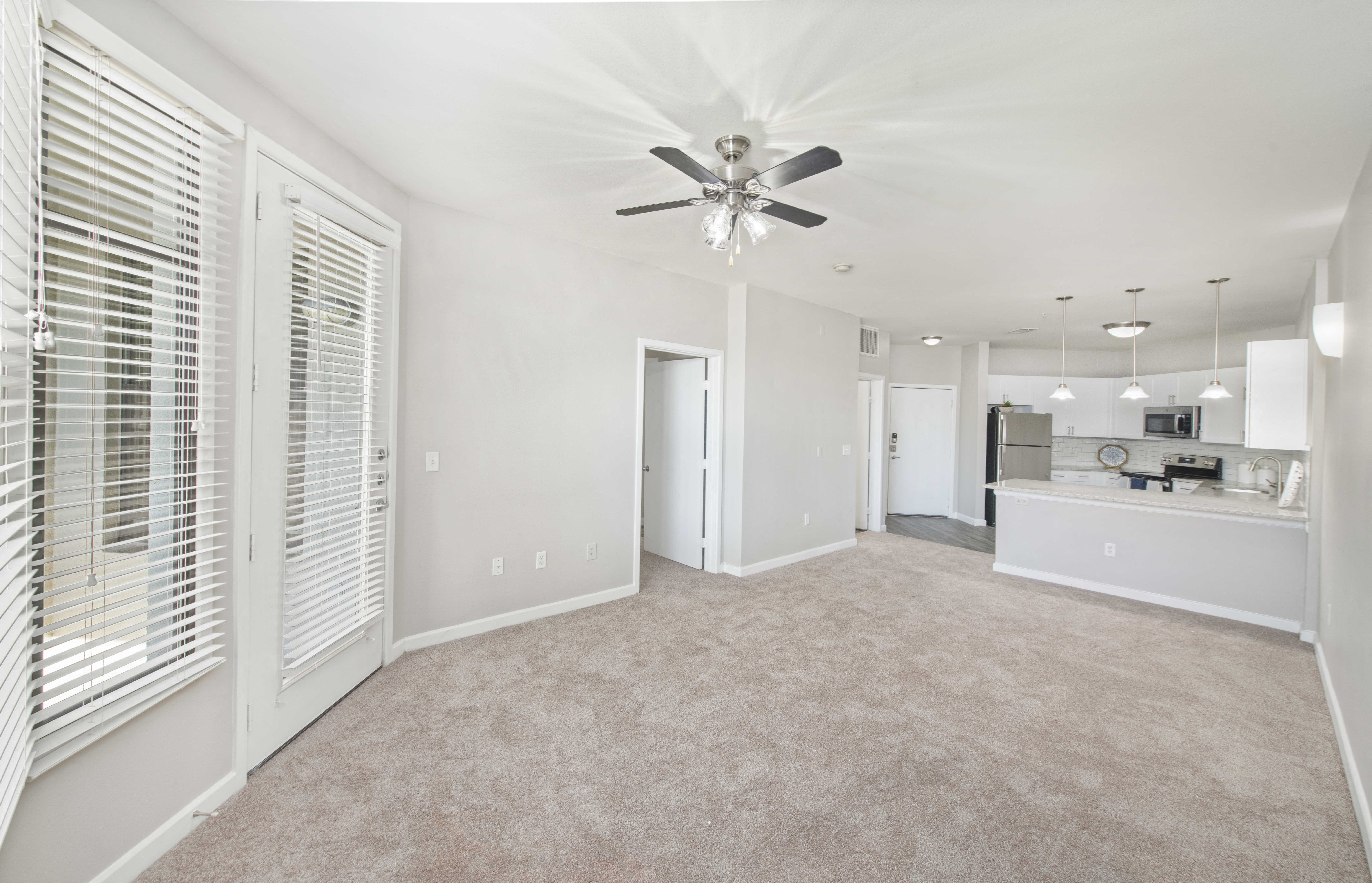 an empty living room with a ceiling fan and a kitchen
