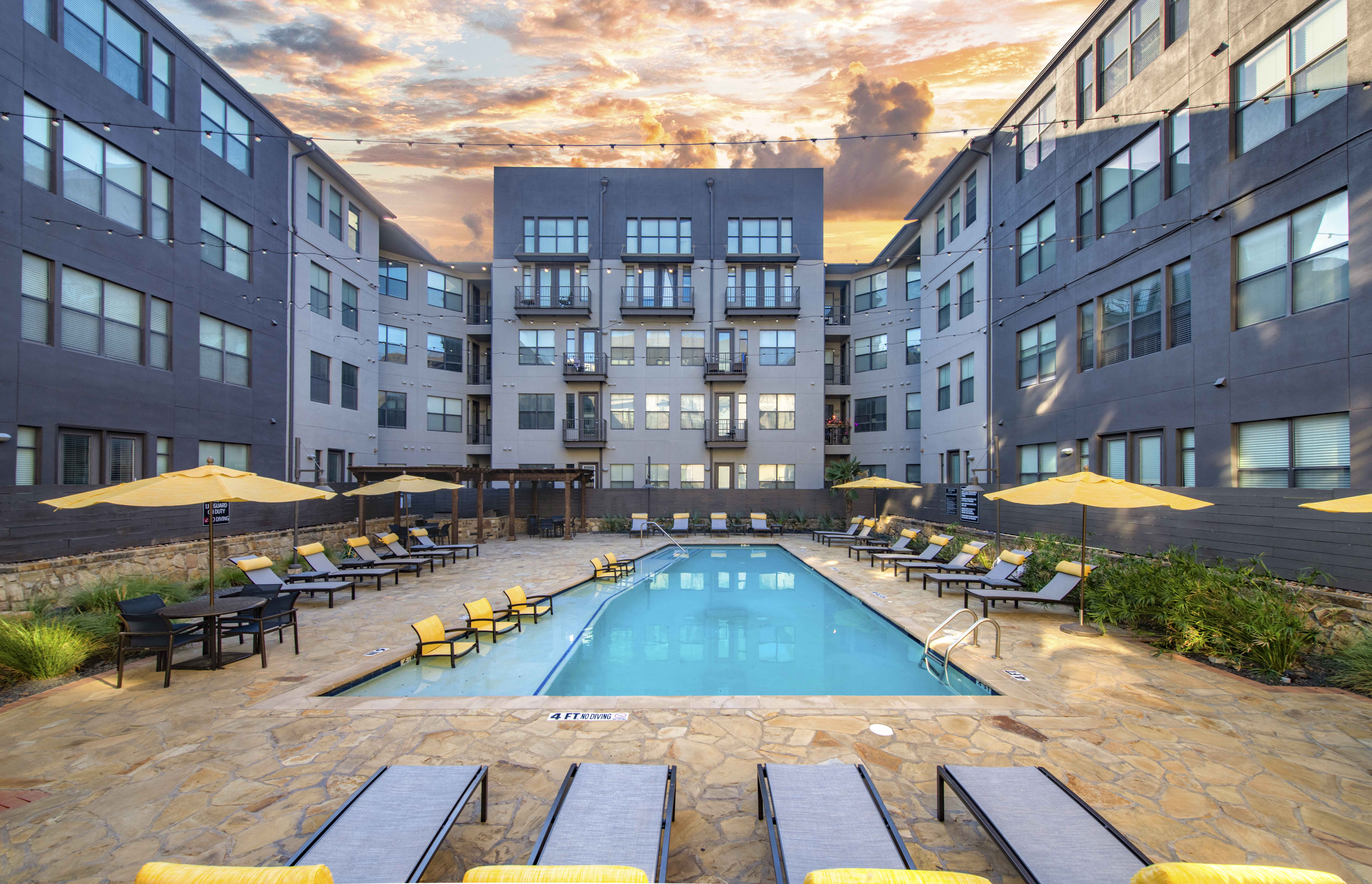 a swimming pool in the middle of an apartment building with yellow umbrellas