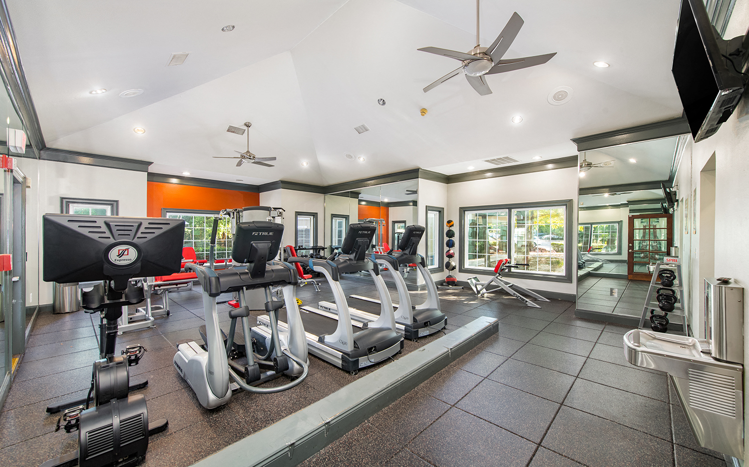 a gym with cardio machines and a ceiling fan