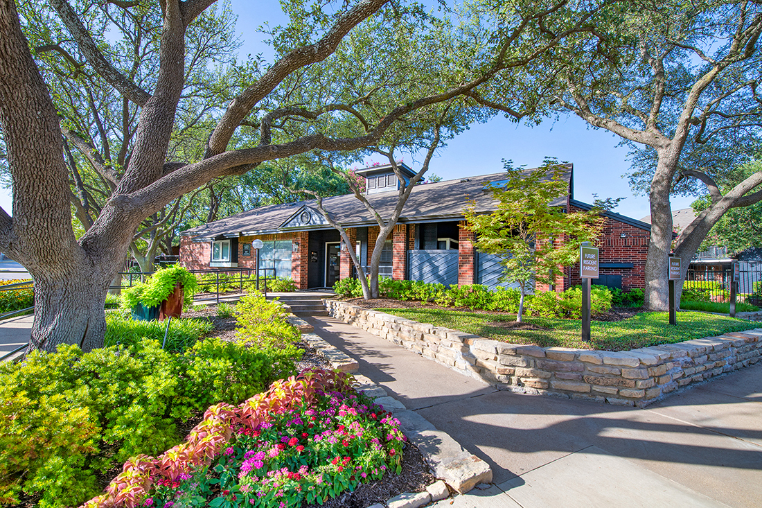 the front yard of a house with a stone retaining wall and trees