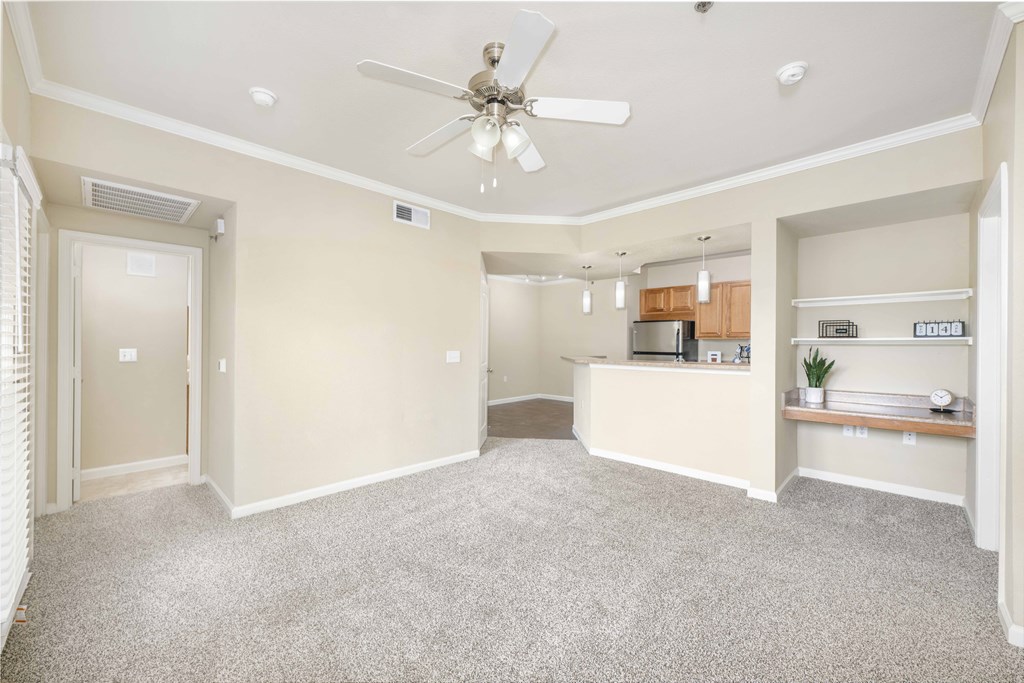 an empty living room with a ceiling fan and a kitchen
