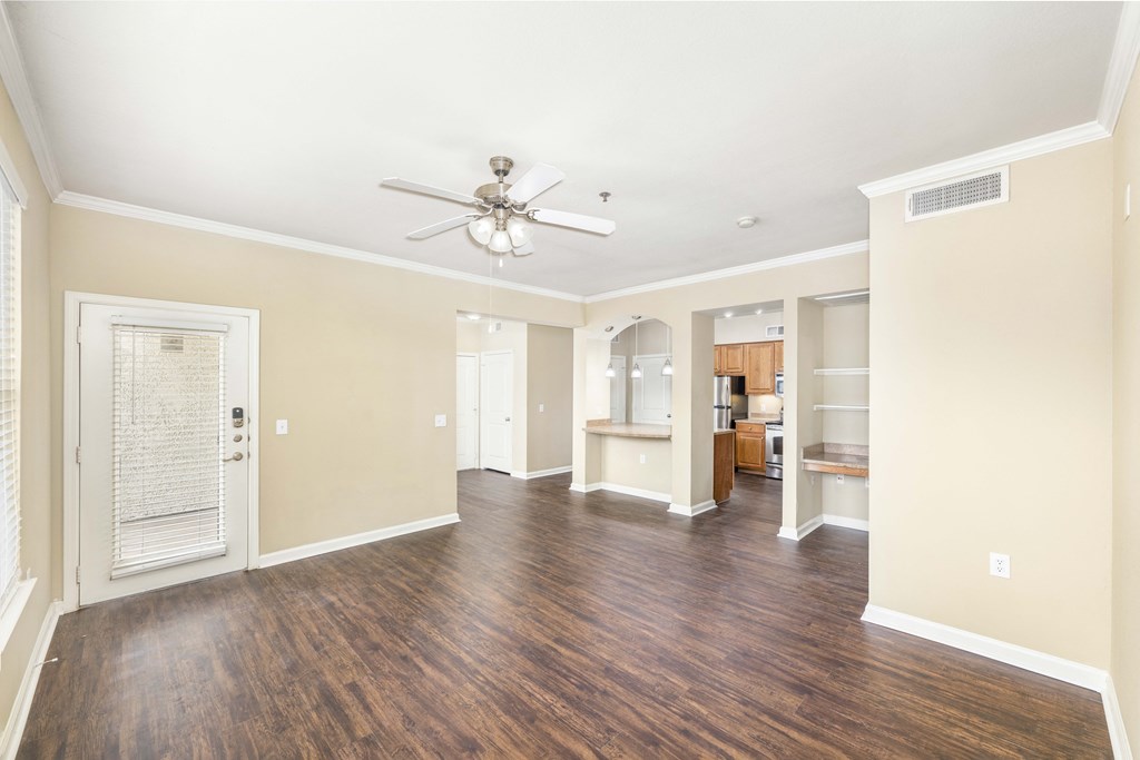 an empty living room with a ceiling fan and a door to a kitchen