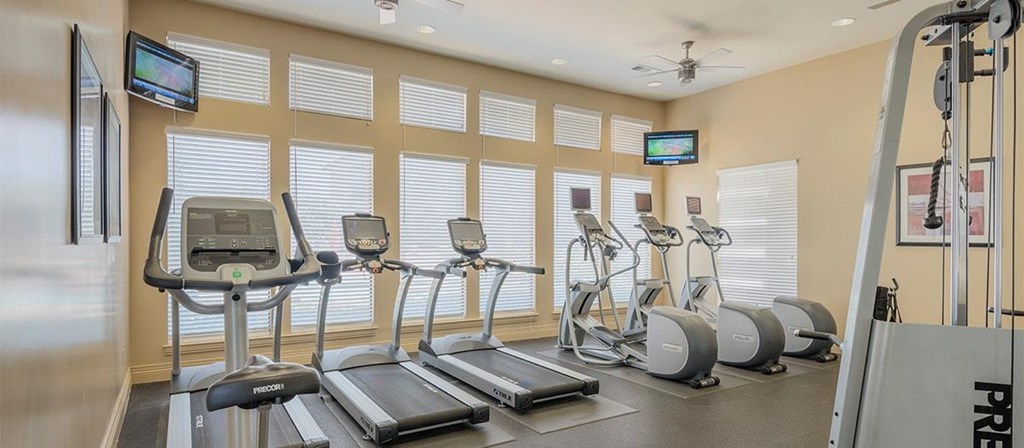 a gym with various cardio machines and televisions