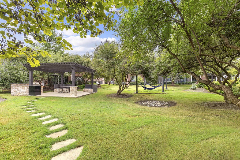 A gazebo is surrounded by a well-kept lawn and trees.